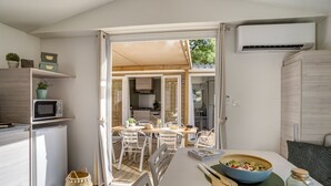 A modern kitchen with white appliances, a dining area with a table and chairs, and an open layout leading to a balcony. - Camping Le Bois Fleuri (Argelès-sur-Mer)