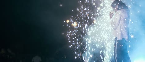Una persona de pie en un escenario con fuegos artificiales al fondo.