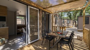 A covered outdoor patio with a table and chairs, a wooden deck, and a view of a neighboring house. - Camping Le Bois Fleuri (Argelès-sur-Mer)