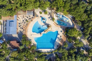 An aerial view of a resort with multiple swimming pools, sun loungers, and a large building with a flat roof. - Camping Le Bois Fleuri (Argelès-sur-Mer)