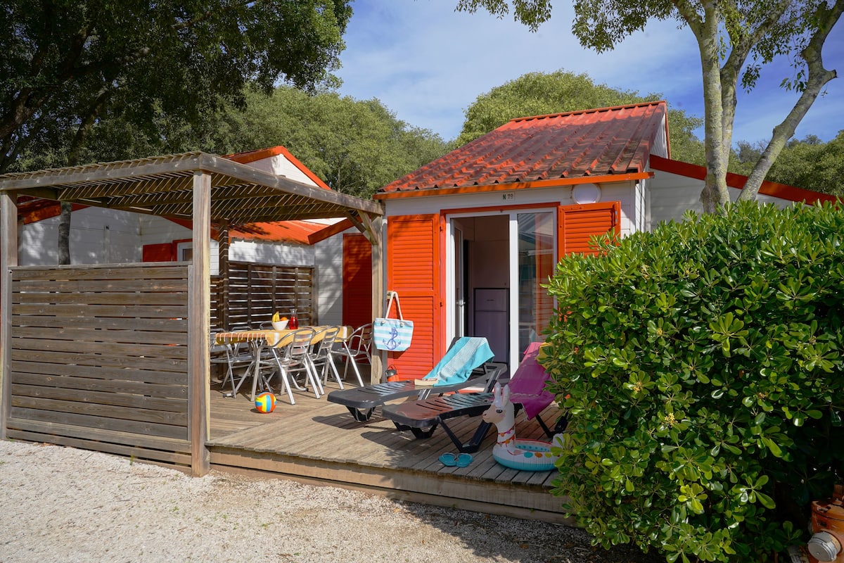 Um pequeno edifício com telhado vermelho, varanda coberta, área de estar ao ar livre e piscina.