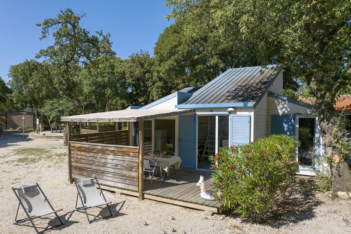 Um pequeno edifício térreo com varanda coberta e deck, cercado por árvores.