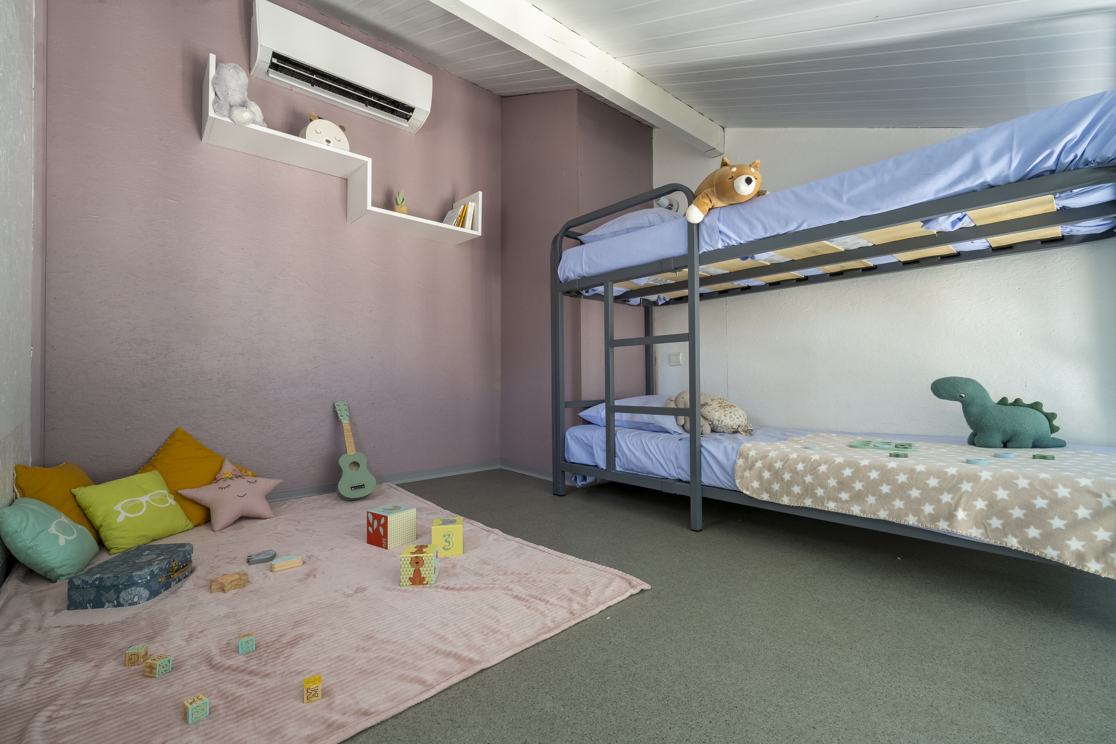 Habitación con literas, una pared rosa, una guitarra y varios juguetes en el suelo.
