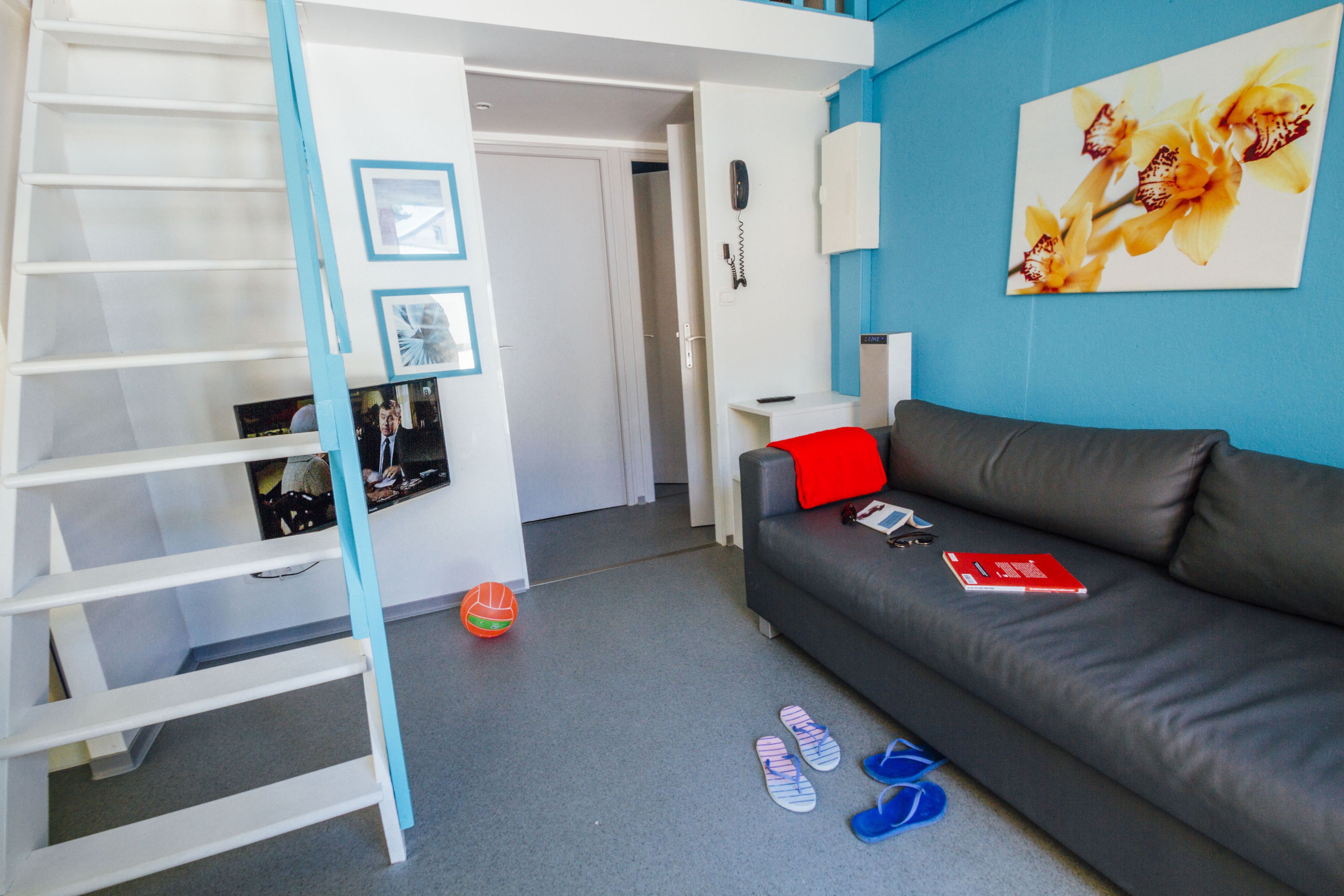 A modern living room with a grey sofa, a red pillow, a white desk, and a blue wall.