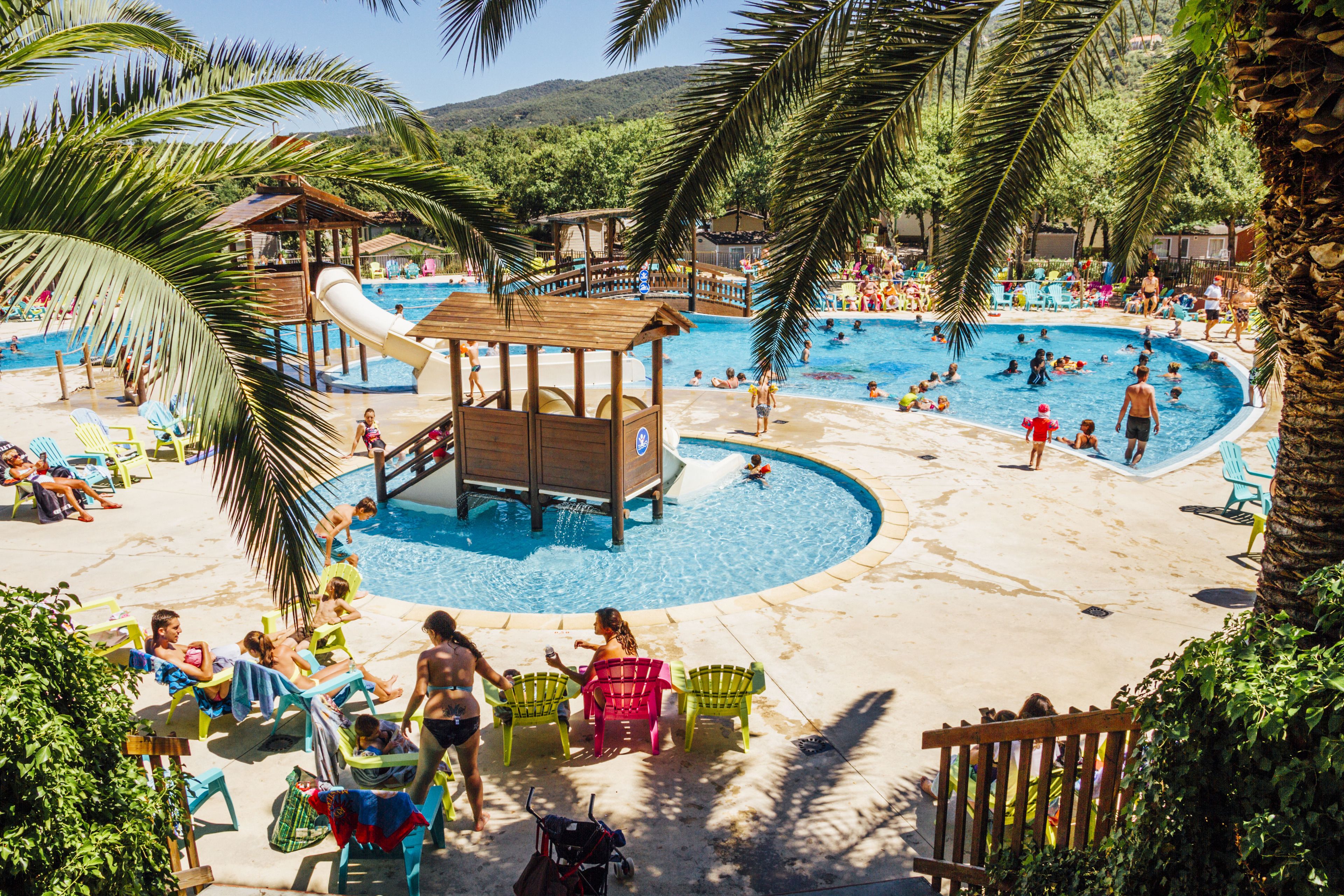 Ein Poolbereich mit mehreren Schwimmbecken, Liegestühlen und einer Wasserrutsche.