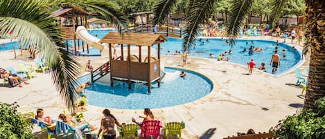 Ein Poolbereich mit mehreren Schwimmbecken, Liegestühlen und einer Wasserrutsche.