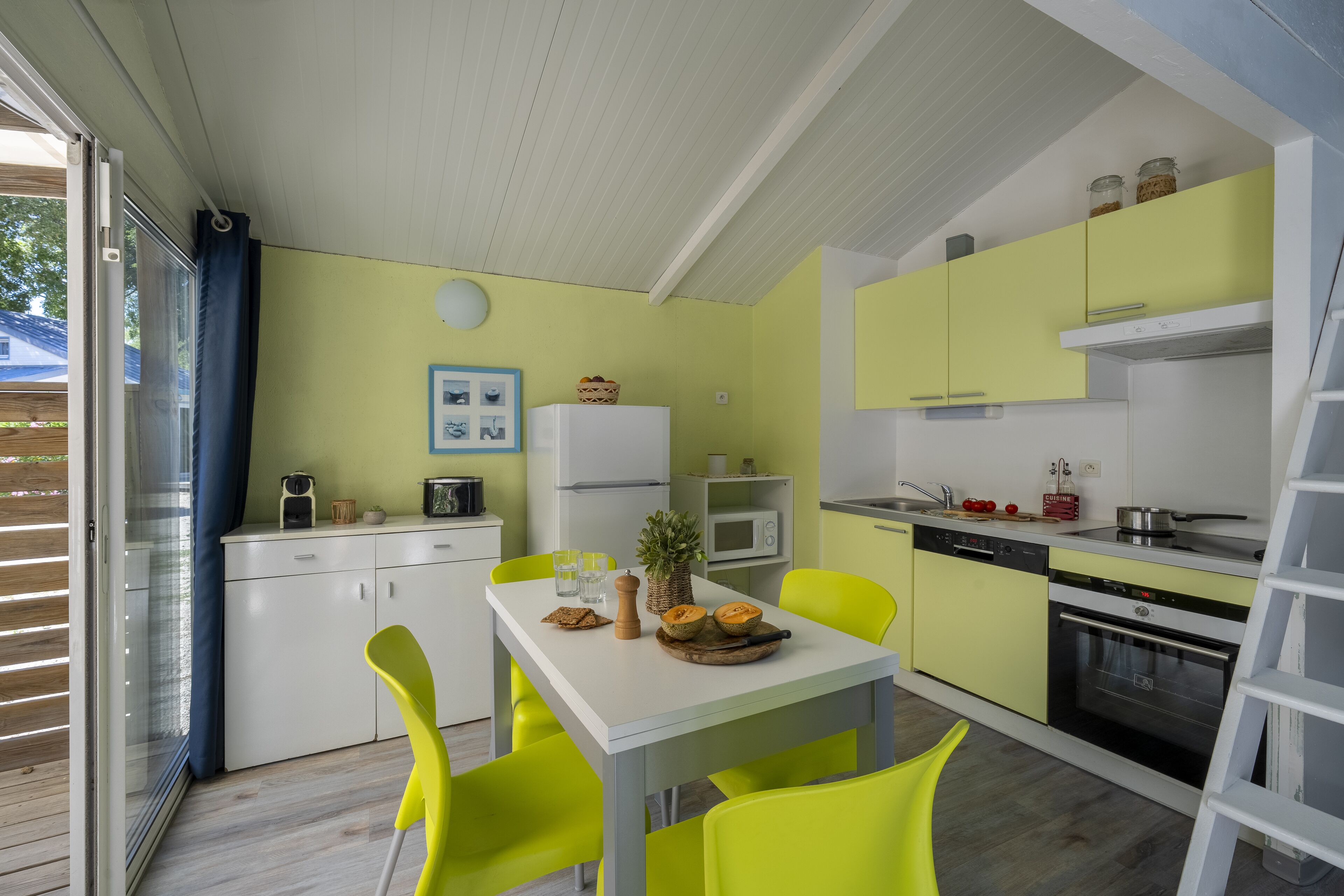 Una cocina compacta con una mesa blanca, sillas amarillo brillante y un microondas.