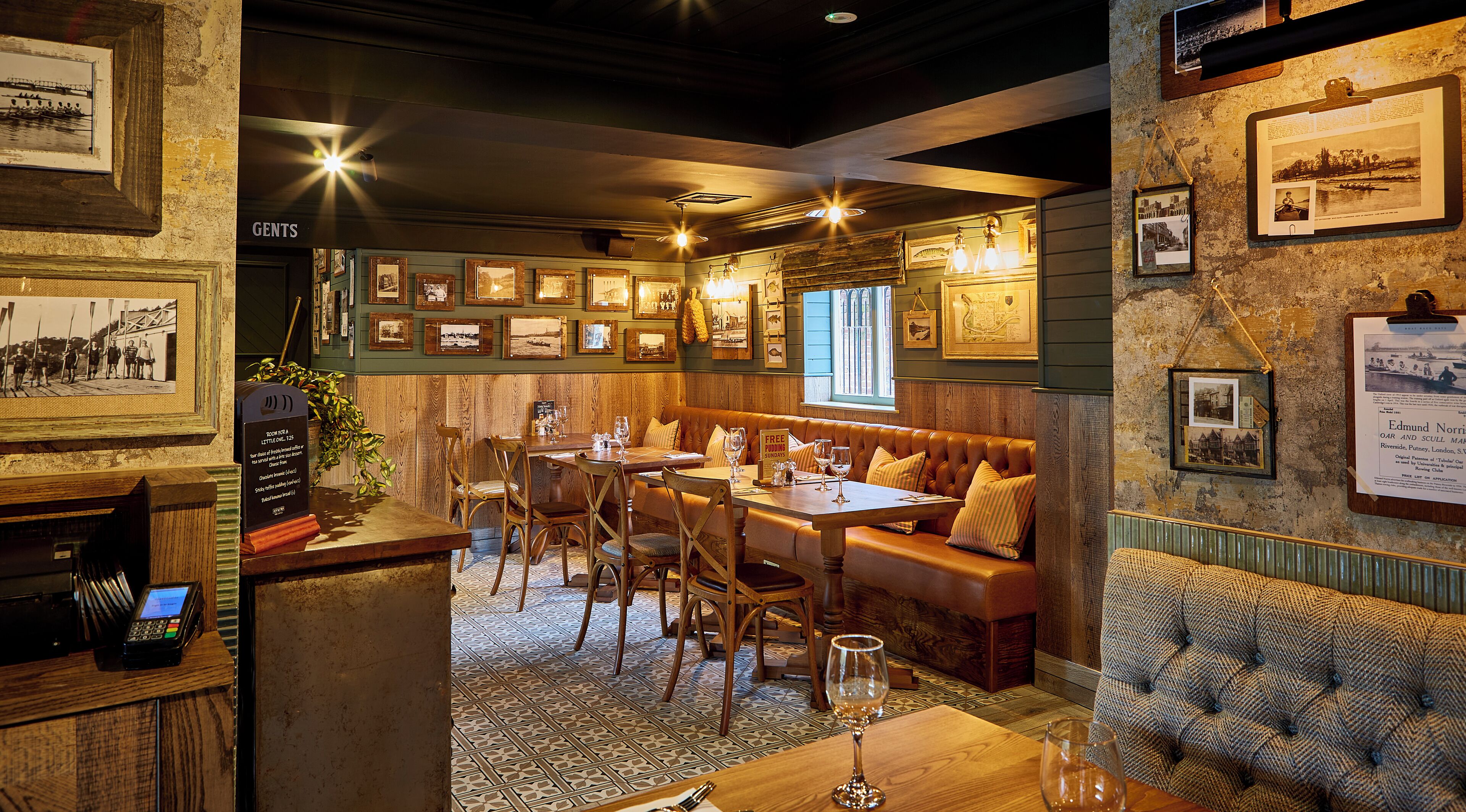 A cozy restaurant with wooden furniture, framed pictures on the walls, and a bar area with a cash register.