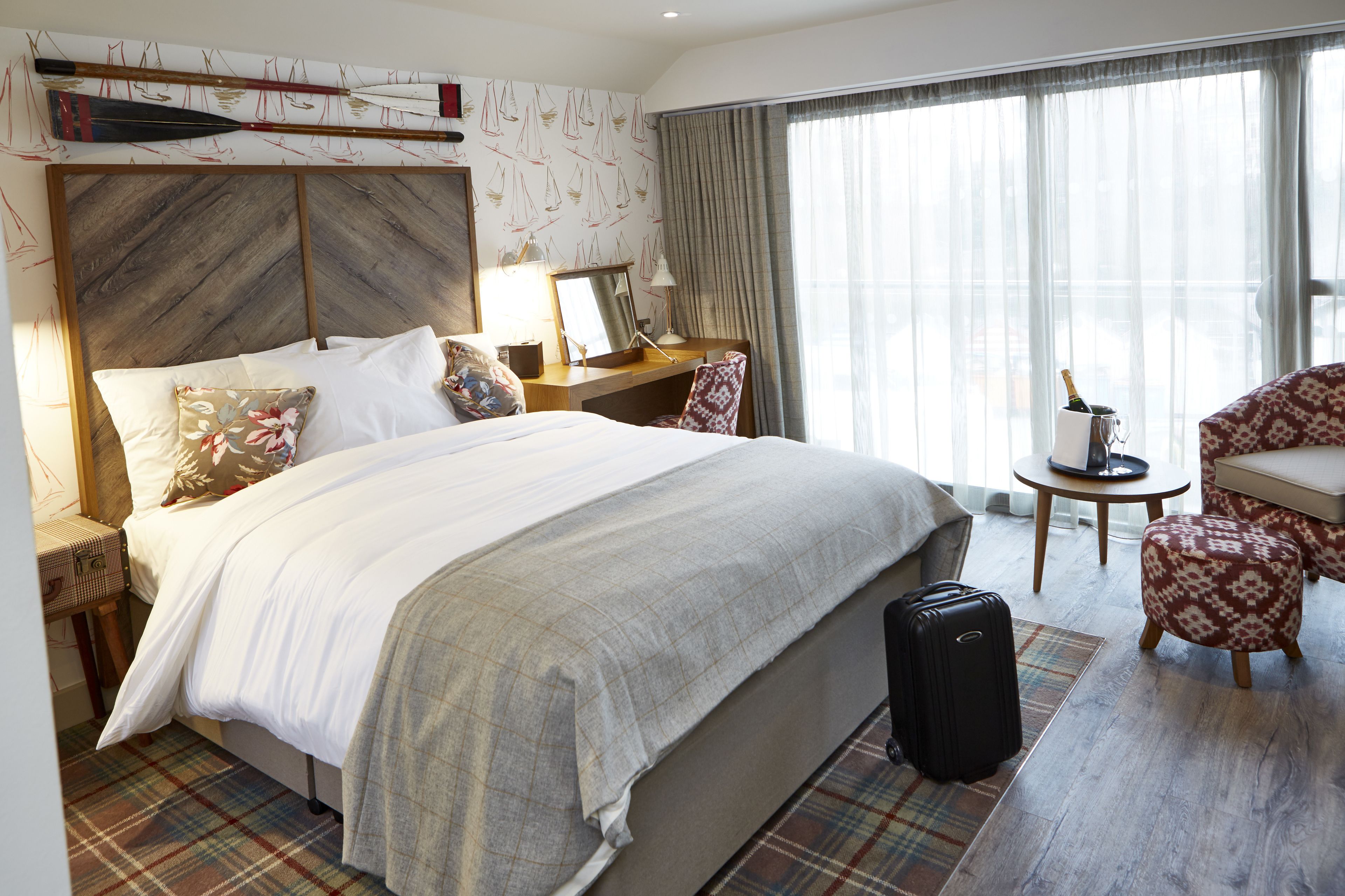 Une chambre d’hôtel avec un grand lit, un bureau, une chaise, une petite table avec une bouteille et une valise.
