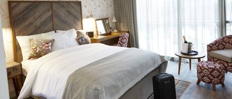 Une chambre d’hôtel avec un grand lit, un bureau, une chaise, une petite table avec une bouteille et une valise.