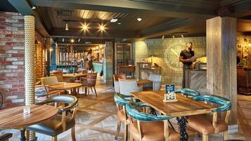 A restaurant interior with brick walls, wooden tables and chairs, and a bar area.