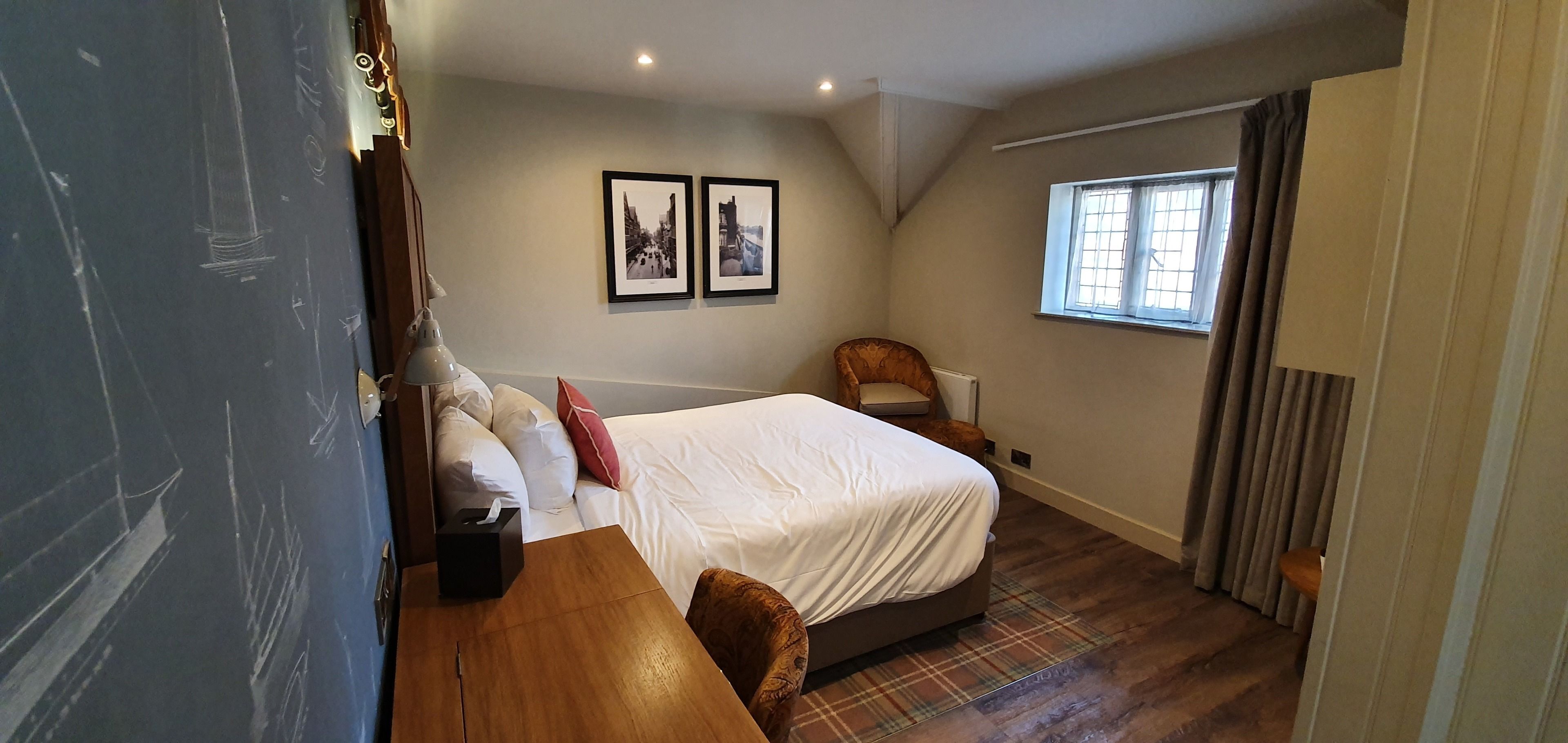A bedroom with a bed, a desk, a chair, a window, and two framed pictures on the wall.