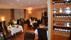 A dining area with tables set for two, a wine rack with bottles, and a chandelier. - Fasil International Hotel (Addis Ababa)