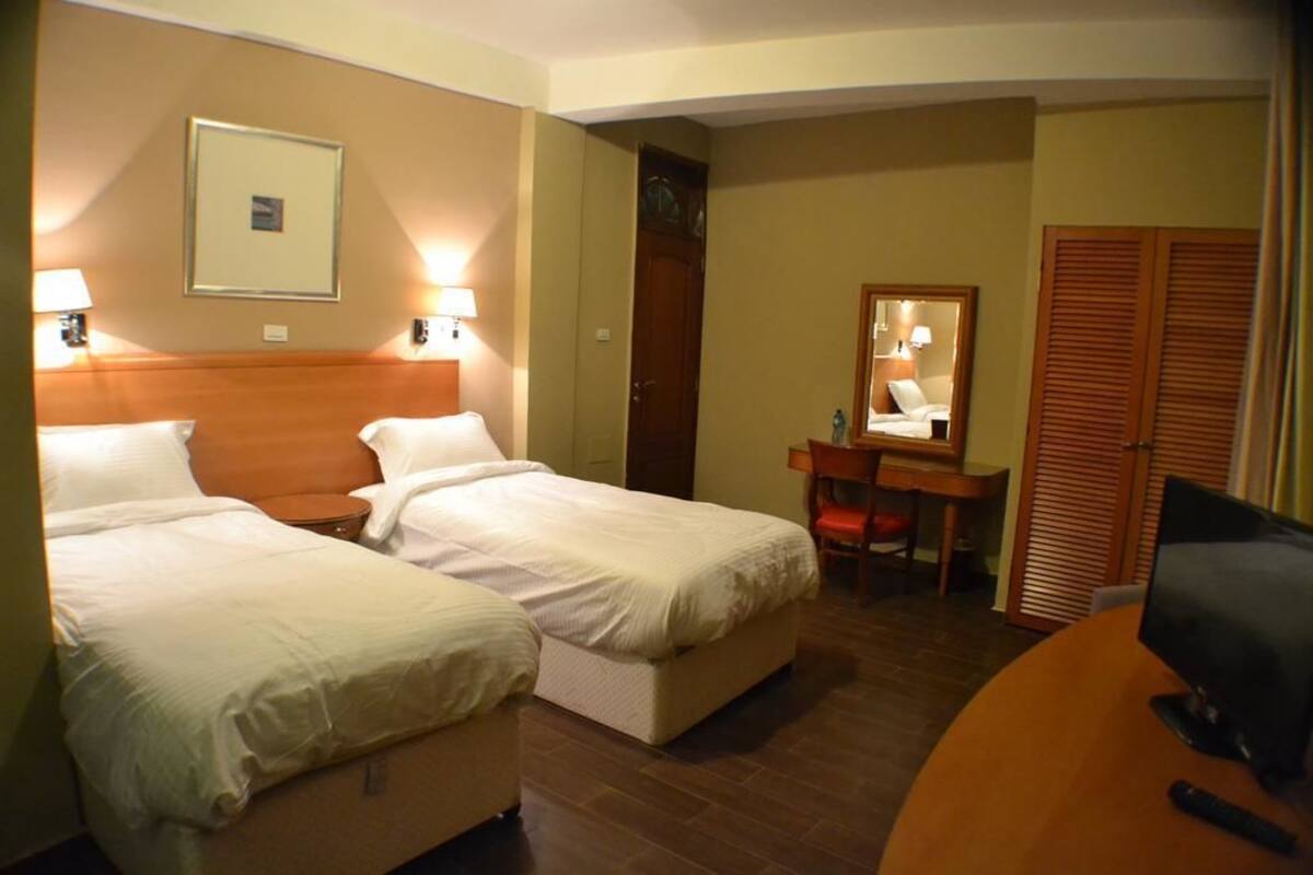 Une chambre d’hôtel avec deux lits, un bureau, une chaise, une télévision et une armoire.