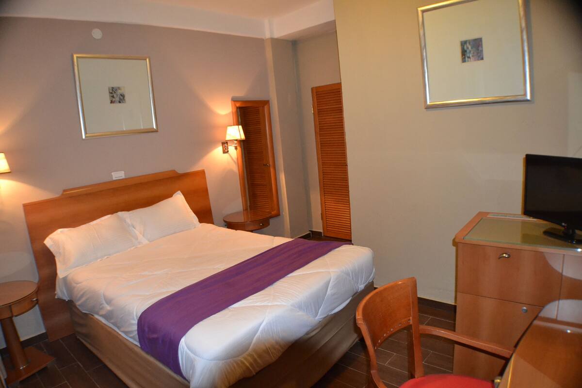 Une chambre d’hôtel comprenant un lit, des tables de chevet, un bureau, une chaise et un téléviseur.