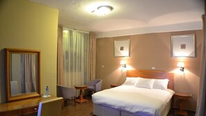 A hotel room with a large bed, two bedside tables, a desk with a chair, a small table, and a mirror. - Fasil International Hotel (Addis Ababa)