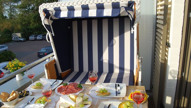 Una mesa de comedor dispuesta con platos de queso, embutidos y frutas, junto a una zona de estar exterior a rayas.
