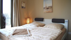 Una habitación de hotel con cama, ventana con cortinas, una lámpara de pared y dos cuadros.