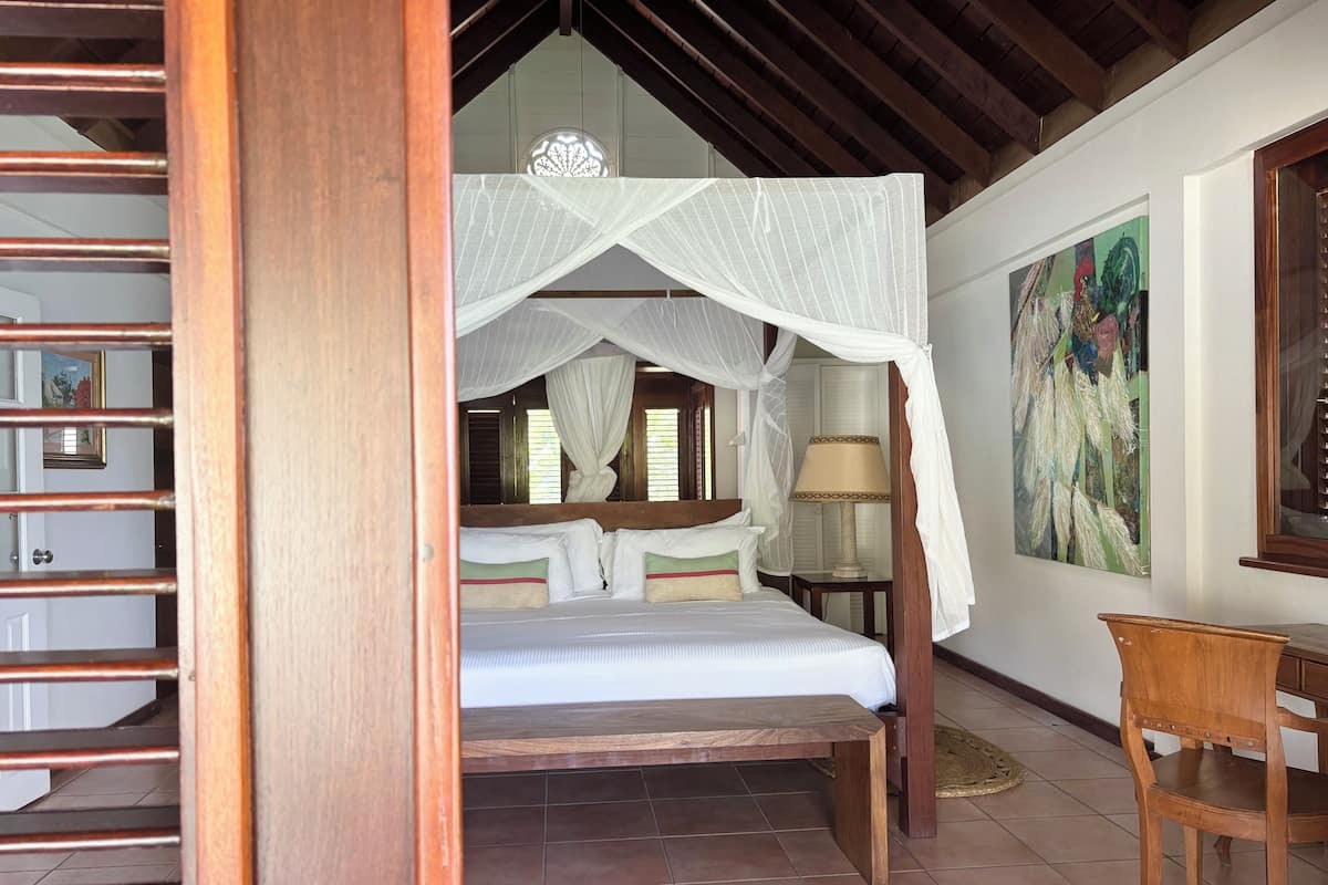 A bedroom with a wooden bed, a canopy, a nightstand, a lamp, and a chair.