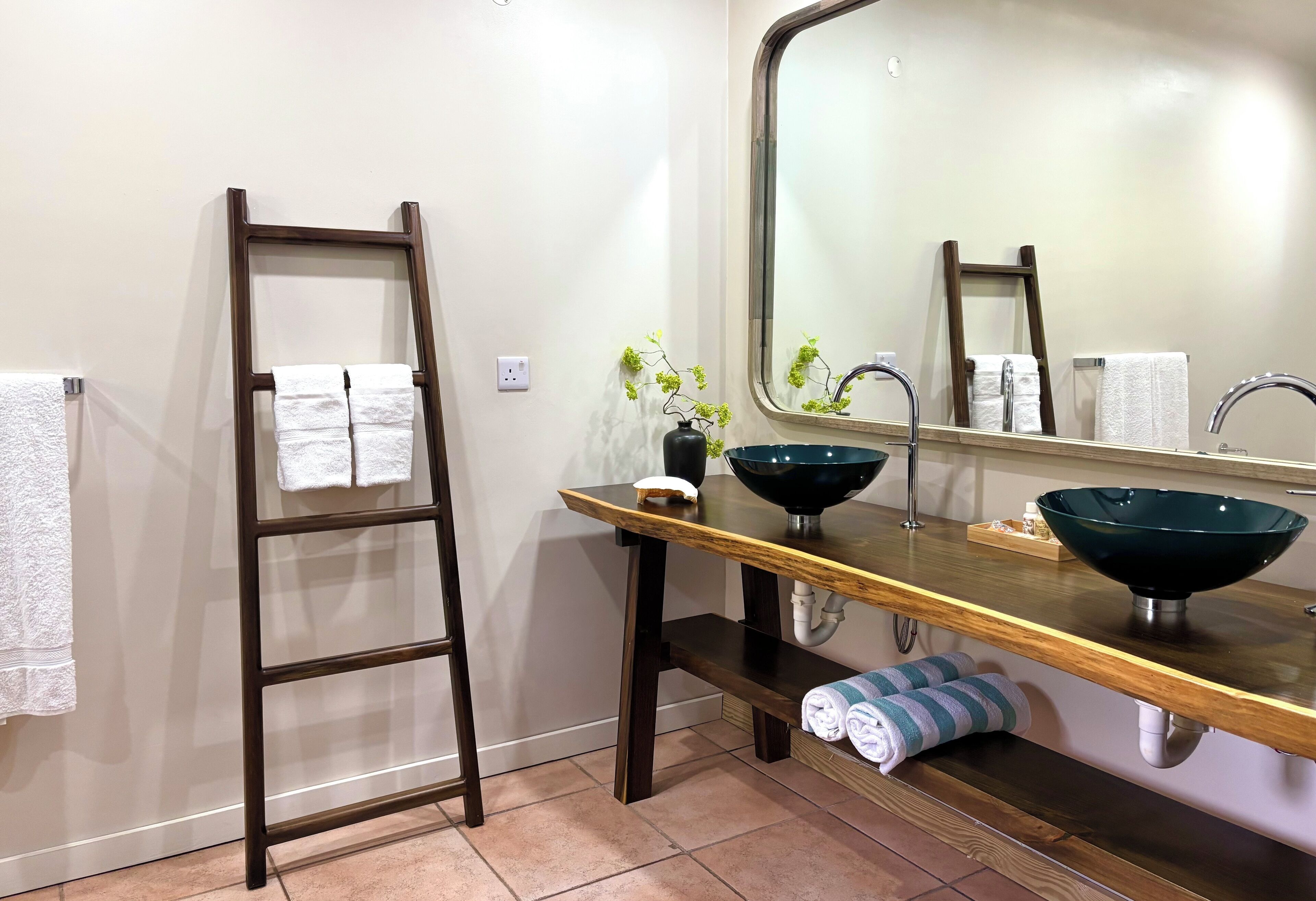 A bathroom with a wooden ladder, two sinks, a mirror, and towels.