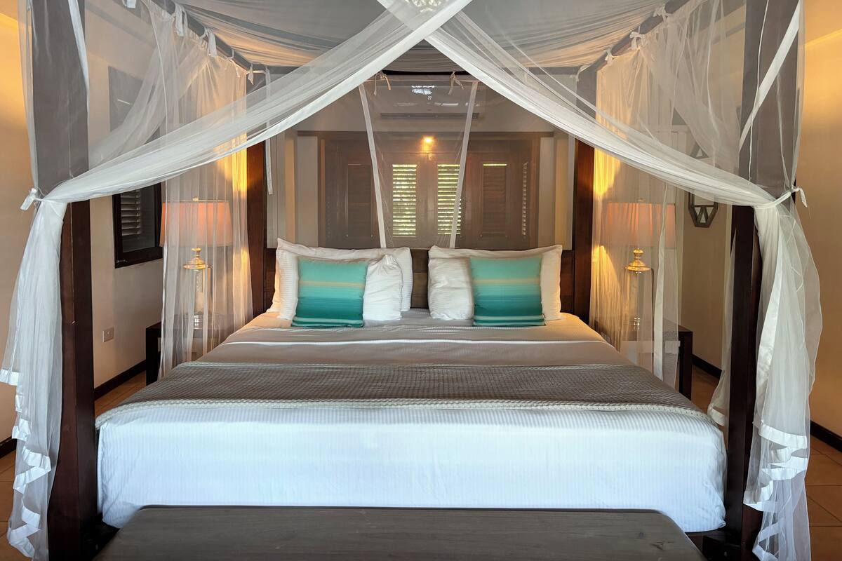 A bed with a canopy, white bedding, and two pillows with a teal gradient.