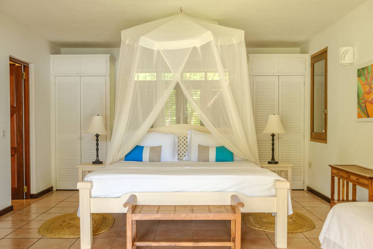 A bedroom with a canopy bed, white walls, and a wooden bench.