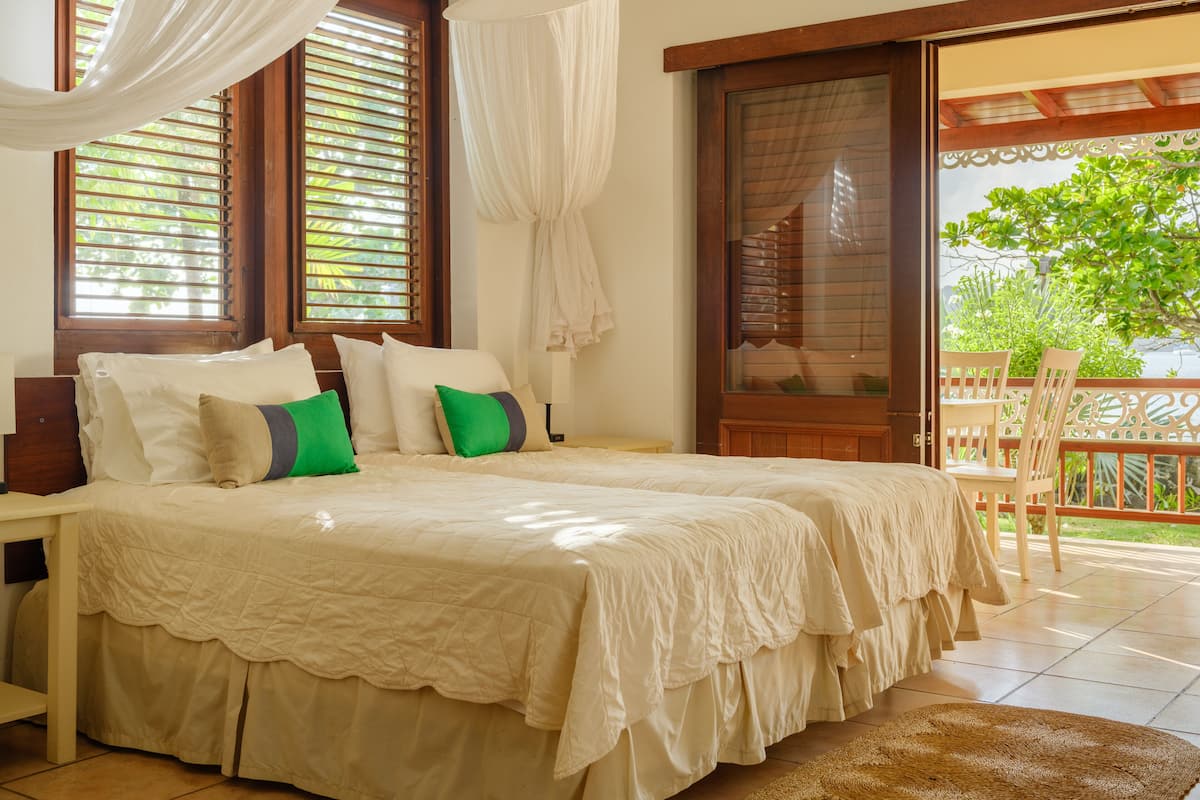A bedroom with a large bed, a wooden chair, and a view of greenery outside.