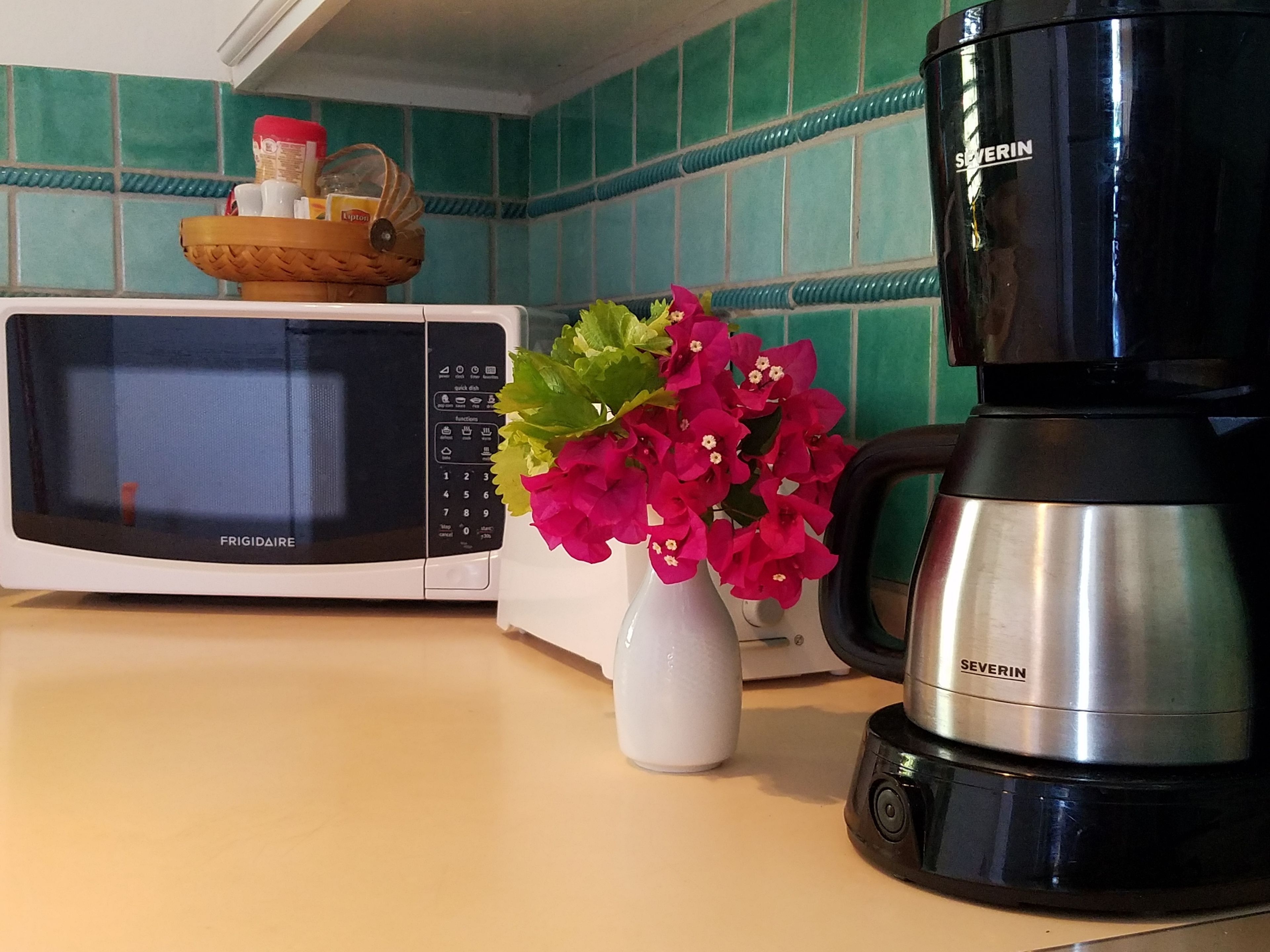 A kitchen with a white microwave, a black coffee maker, and a vase with pink flowers on the counter.