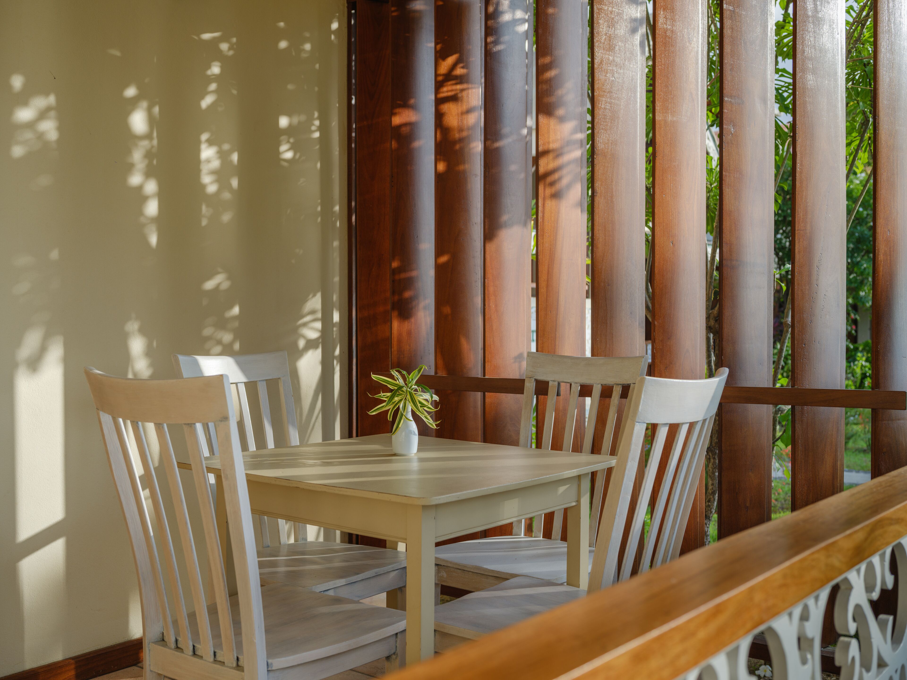 A wooden table with four chairs, a small potted plant, and a wooden bench.
