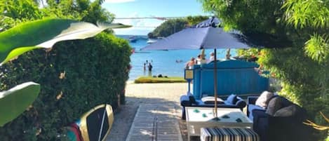 A beachside lounge area with a view of the sea, a covered seating area, and a surfboard rack.