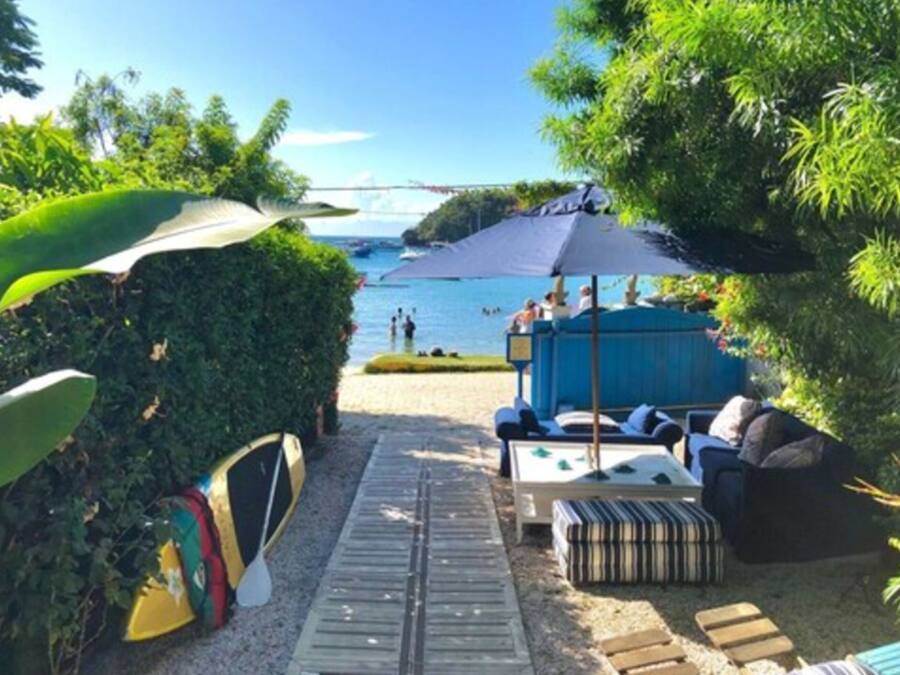 Un espace de détente aménagé au bord de la plage, offrant une vue sur la mer, avec un coin salon abrité et un porte-planches de surf.