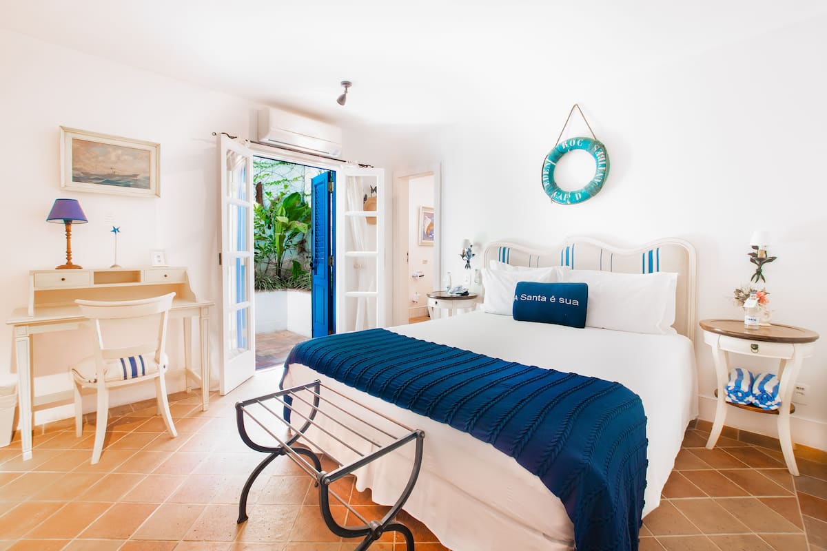 A bedroom with a bed, a desk, a chair, a small table, and a wall-mounted lamp.