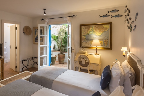 Habitación de hotel con cama, mesita de noche, lámpara, mapa en la pared y plantas en macetas.