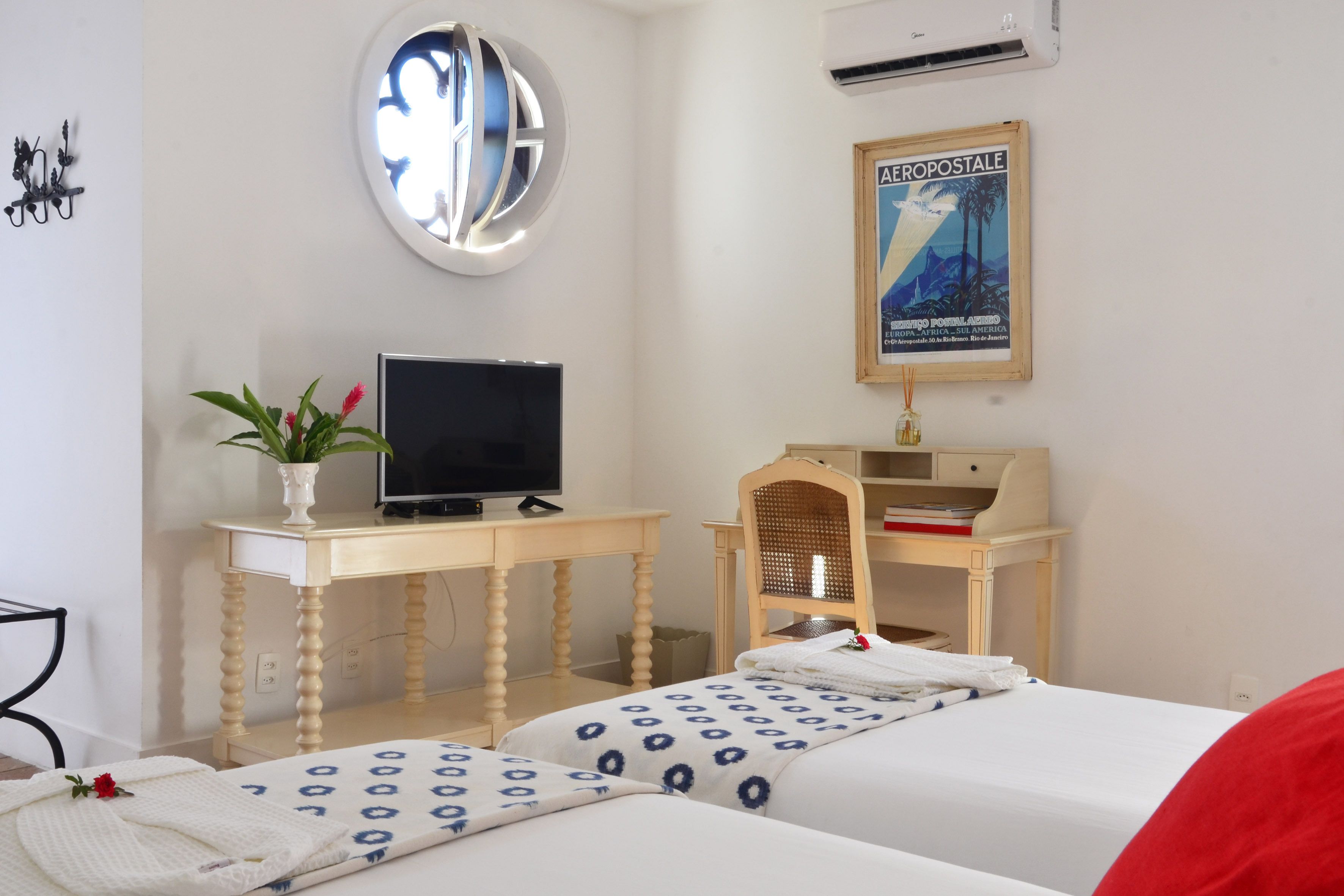 A hotel room with a bed, a desk with a TV, a mirror, and a poster on the wall.