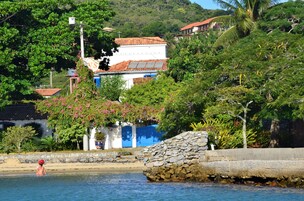 Una casa costera con un muro de piedra y una puerta azul, rodeada de exuberante vegetación y una vista despejada del mar.