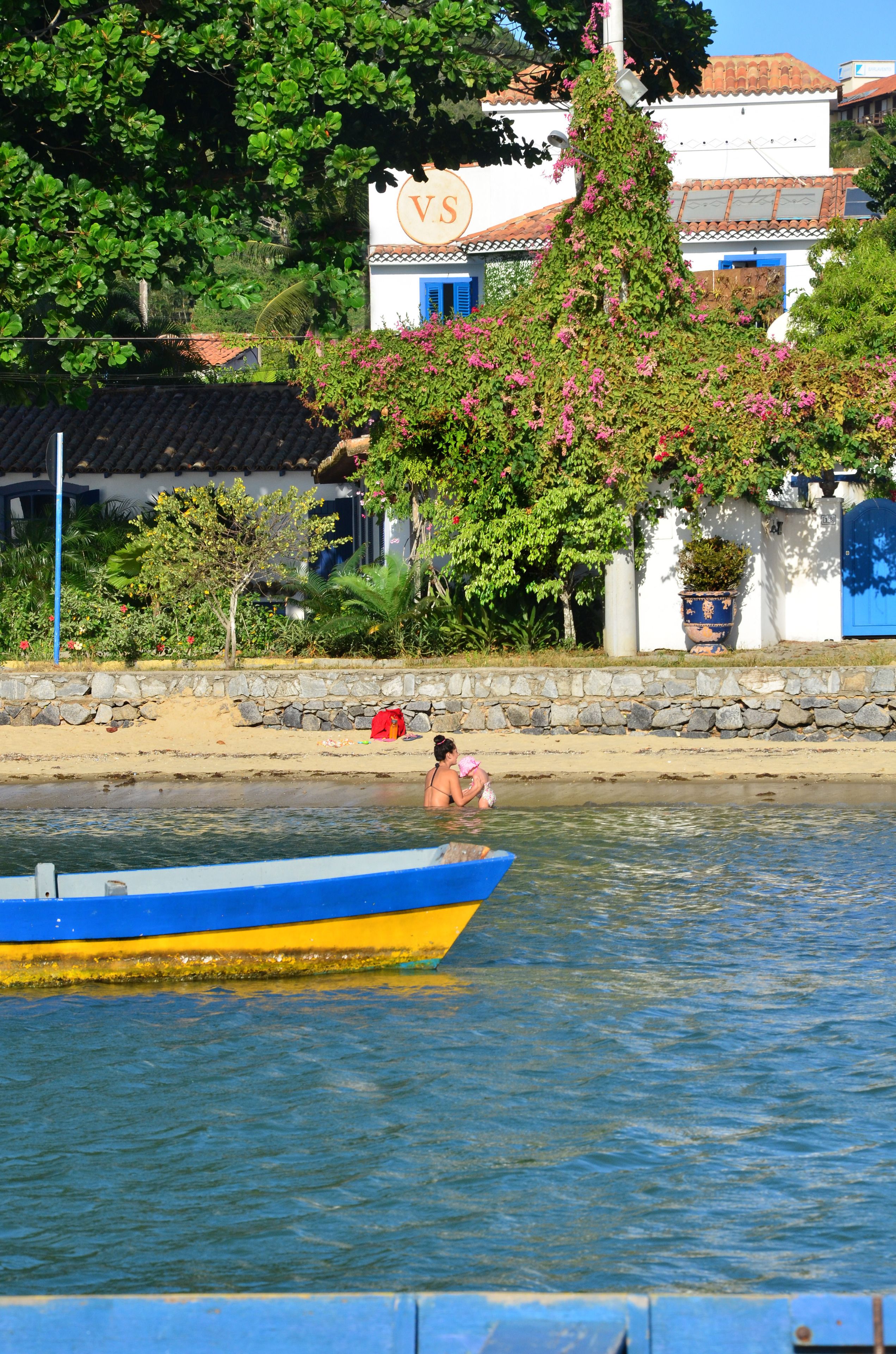 A boat with a blue and yellow hull on calm water, a person in the water, and a building with a 'VS' sign in the background.