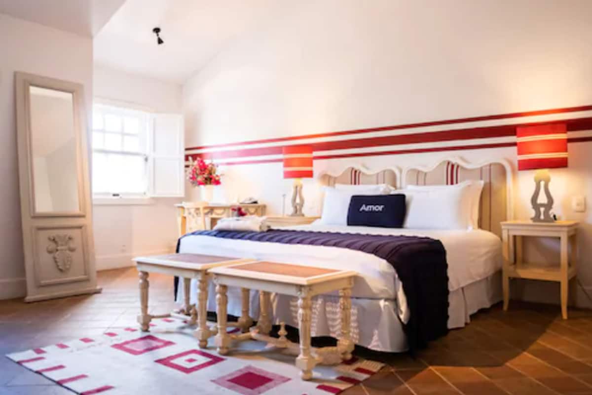 A bedroom with a bed, bedside tables, a nightstand, a mirror, and a window.