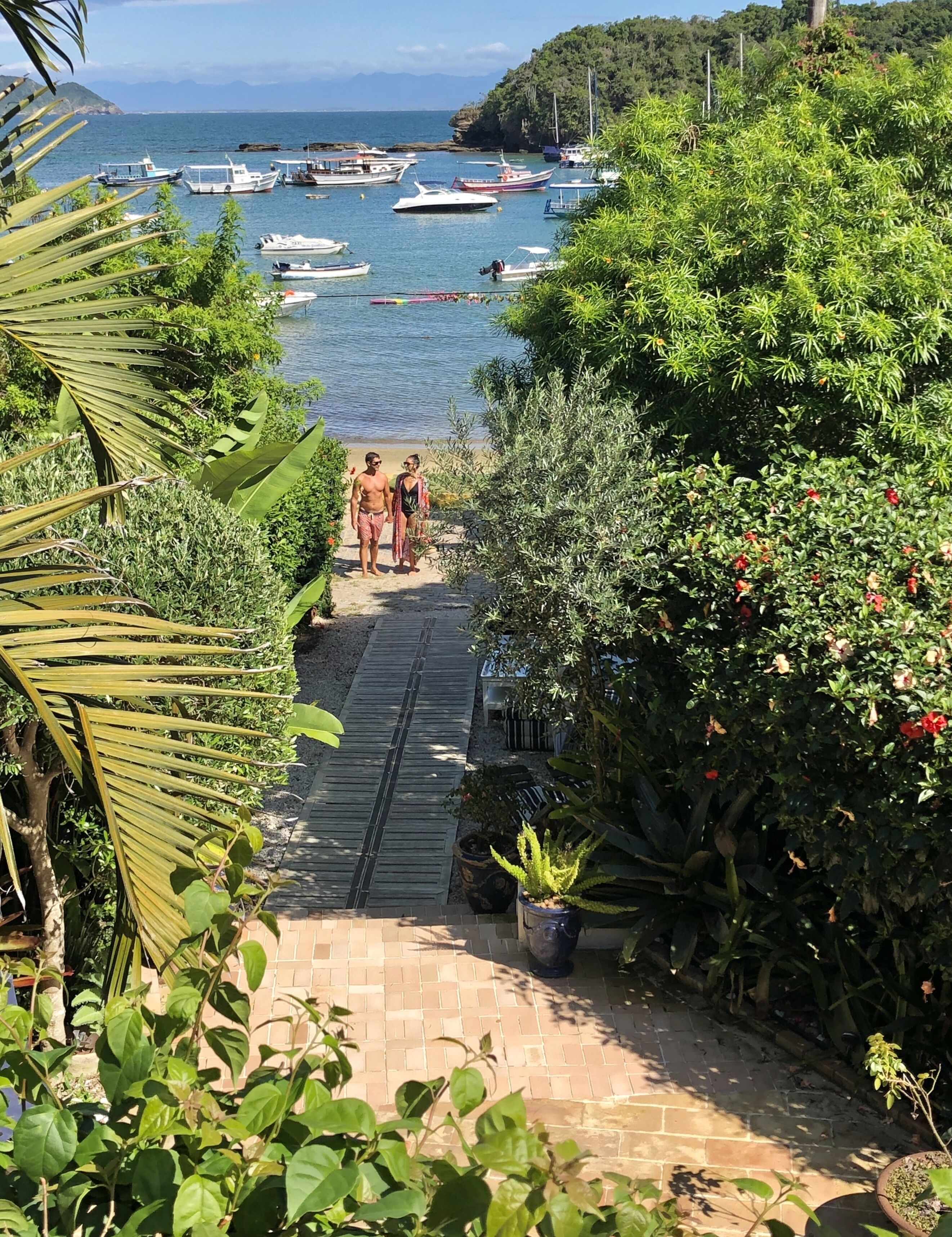 A pathway leading to a beach with boats in the water and lush greenery.