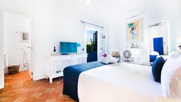 Habitación de hotel con una cama grande, un escritorio con computadora, televisor y ventana con vista a follaje.