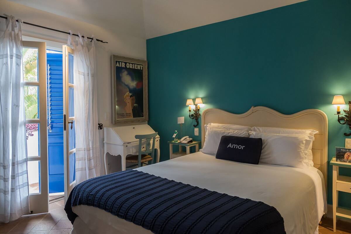 A bedroom with a teal wall, a white bed, and a door with blue shutters.