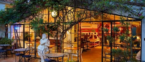 An outdoor café with tables and chairs, surrounded by lush greenery and a decorative archway.