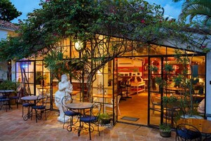 An outdoor café with tables and chairs, surrounded by lush greenery and a decorative archway.