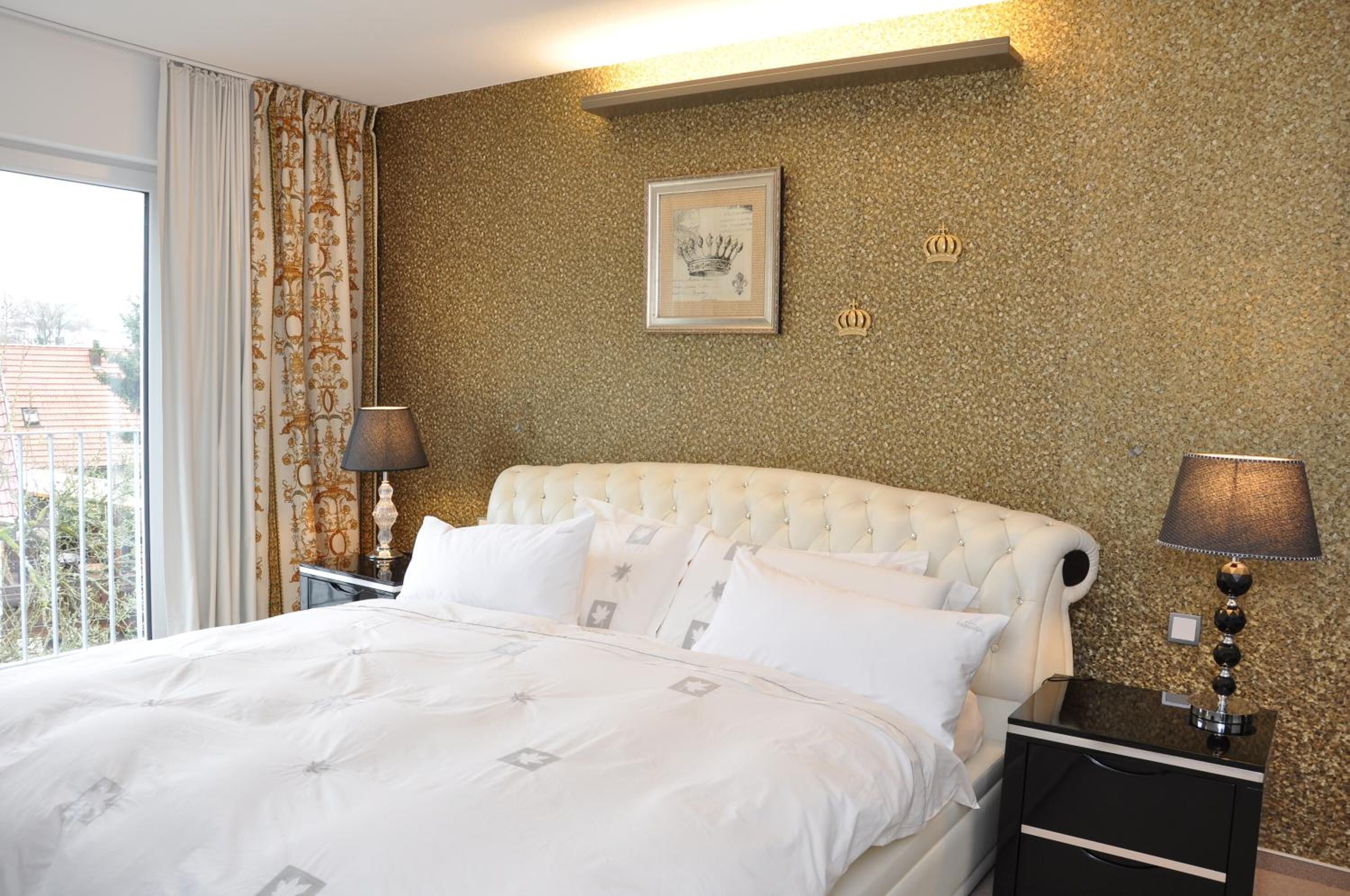 Ein Hotelzimmer mit einer gebügelten Kopfteil, einem großen Bett mit weißer Bettwäsche, zwei Nachttischen mit Lampen, einem gerahmten Bild an der Wand und einem Fenster mit Vorhängen.
