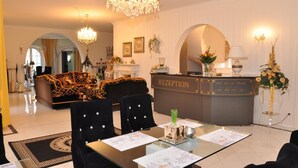A reception area with a reception desk, a chandelier, a sofa, and a dining table with chairs. - Hotel Villa Casamia - Adult Only (Schmalkalden)