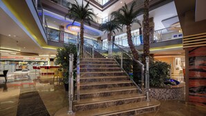 A multi-level atrium with marble stairs, palm trees, and a glass railing.