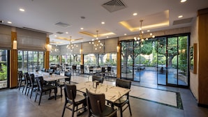 A spacious indoor dining area with multiple tables and chairs, large windows, and ceiling lights.