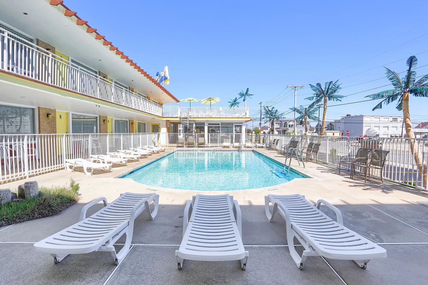 A pool area with lounge chairs, a building with balconies, and palm trees.