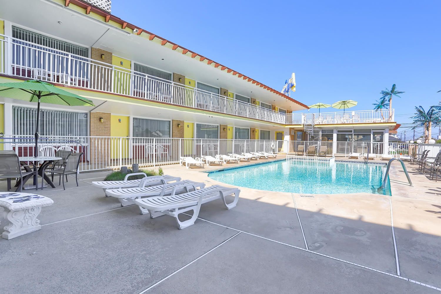 A hotel with a pool area, outdoor seating, and a two-story building with balconies.