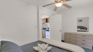 A bedroom with a bed, a dresser, a ceiling fan, and a view into the kitchen. - Ala Kai Motel (Wildwood Crest)