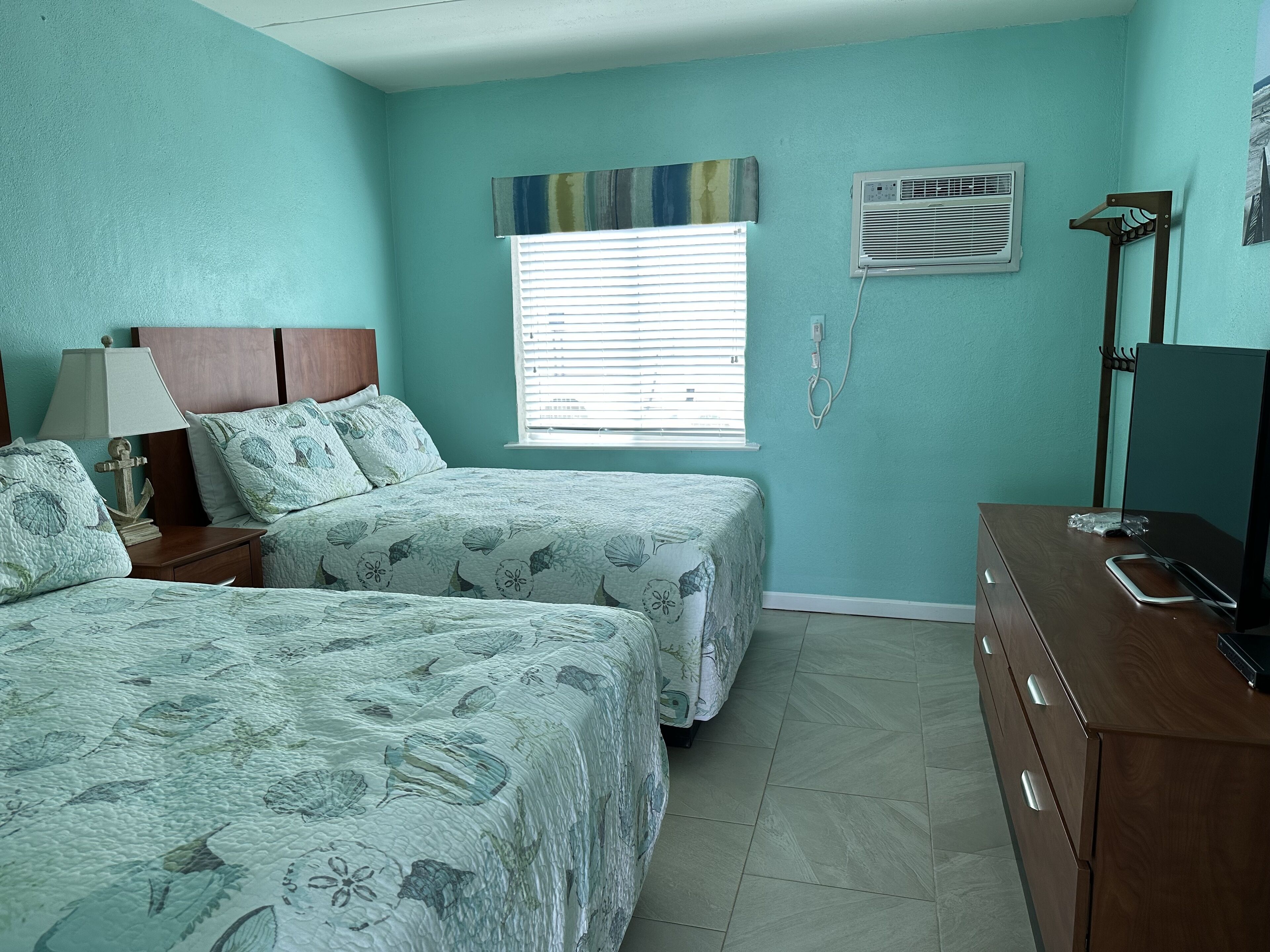 A bedroom with two beds, a dresser, an air conditioner, and a window with blinds.